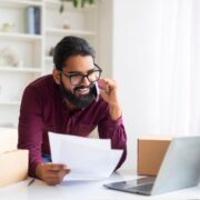 Smiling Indian freelancer verifying shipping documents while on phone call